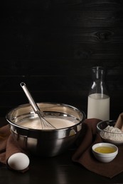 Composition with whisk and dough in bowl on table against dark wooden wall, space for text