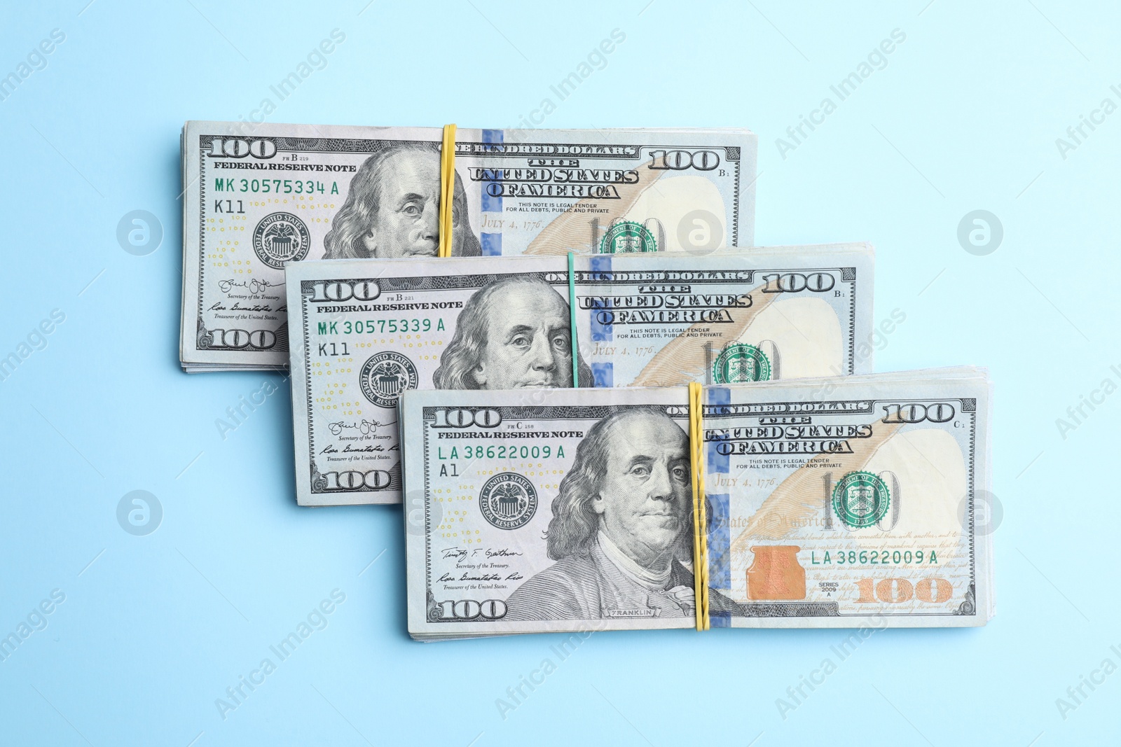 Photo of Bundles of dollar banknotes on light blue background, flat lay