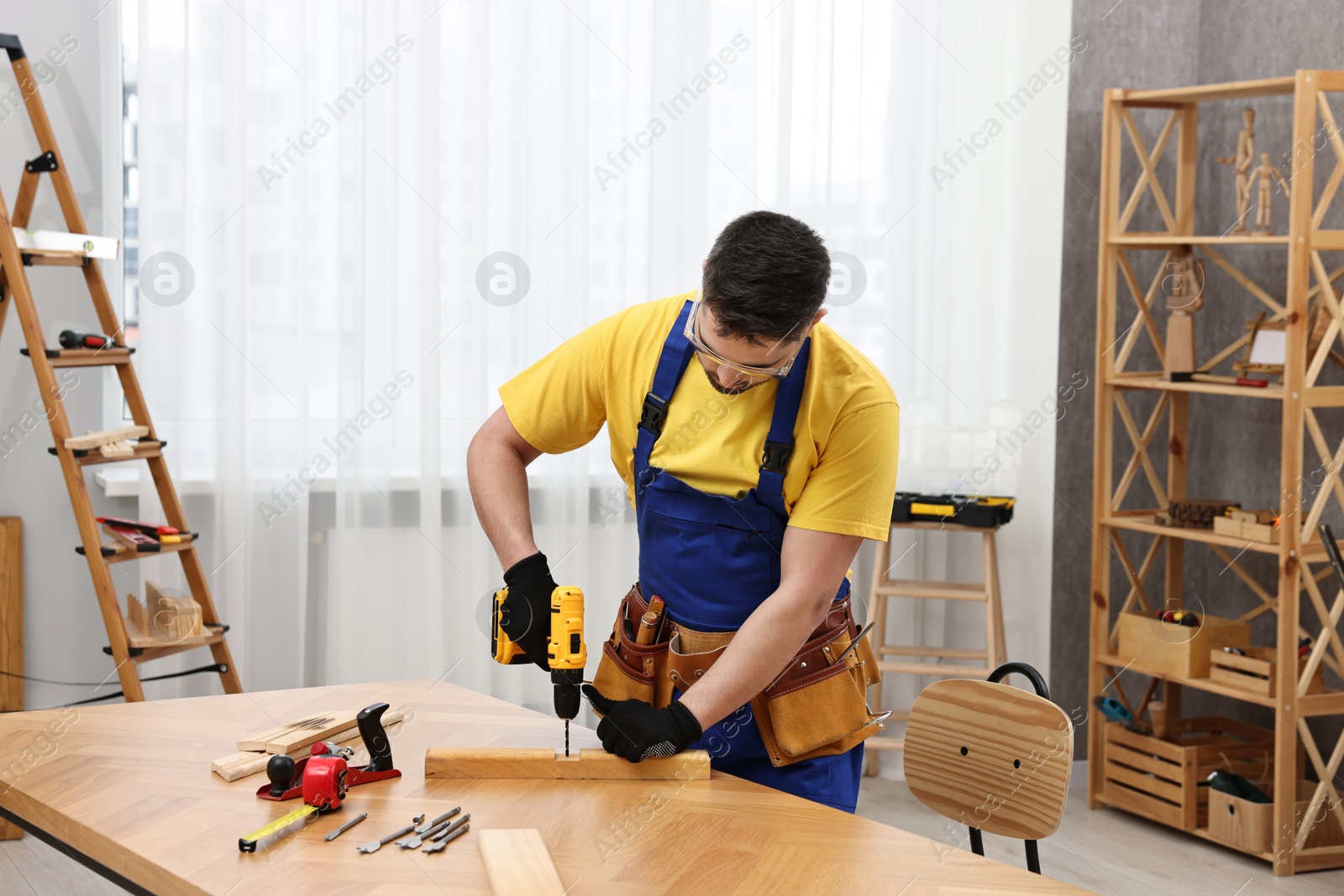 Photo of Young worker using electric drill at table in workshop