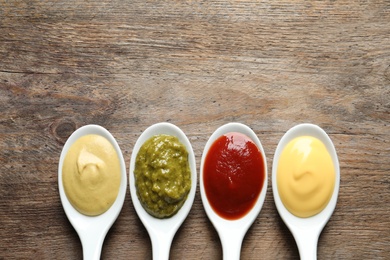 Spoons with different sauces and space for text on wooden background, flat lay