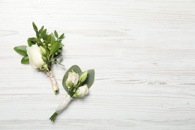 Photo of Wedding stuff. Stylish boutonnieres on white wooden table, top view. Space for text
