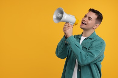 Photo of Special promotion. Young man shouting in megaphone on orange background, space for text
