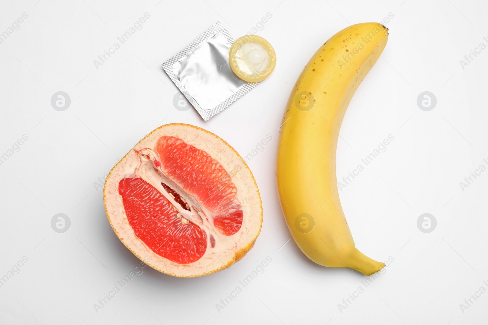 Photo of Condom, cut grapefruit and banana on white background, top view. Safe sex