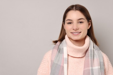 Beautiful woman in warm scarf on gray background, space for text