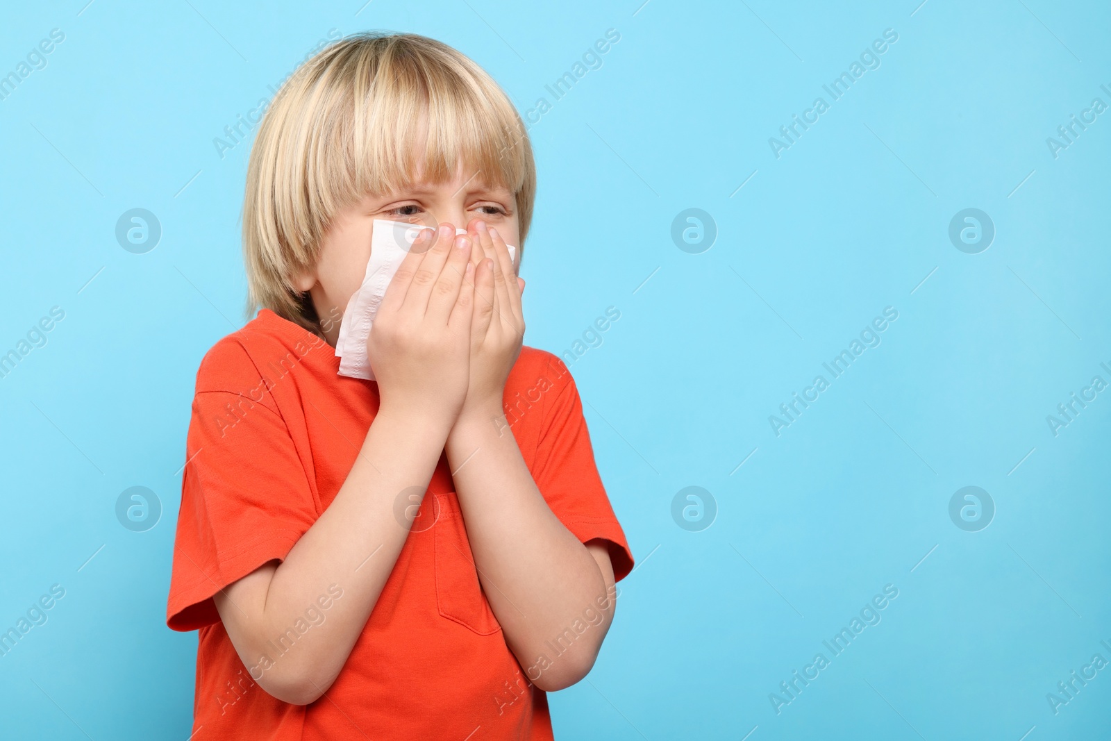 Photo of Boy blowing nose in tissue on light blue background, space for text. Cold symptoms