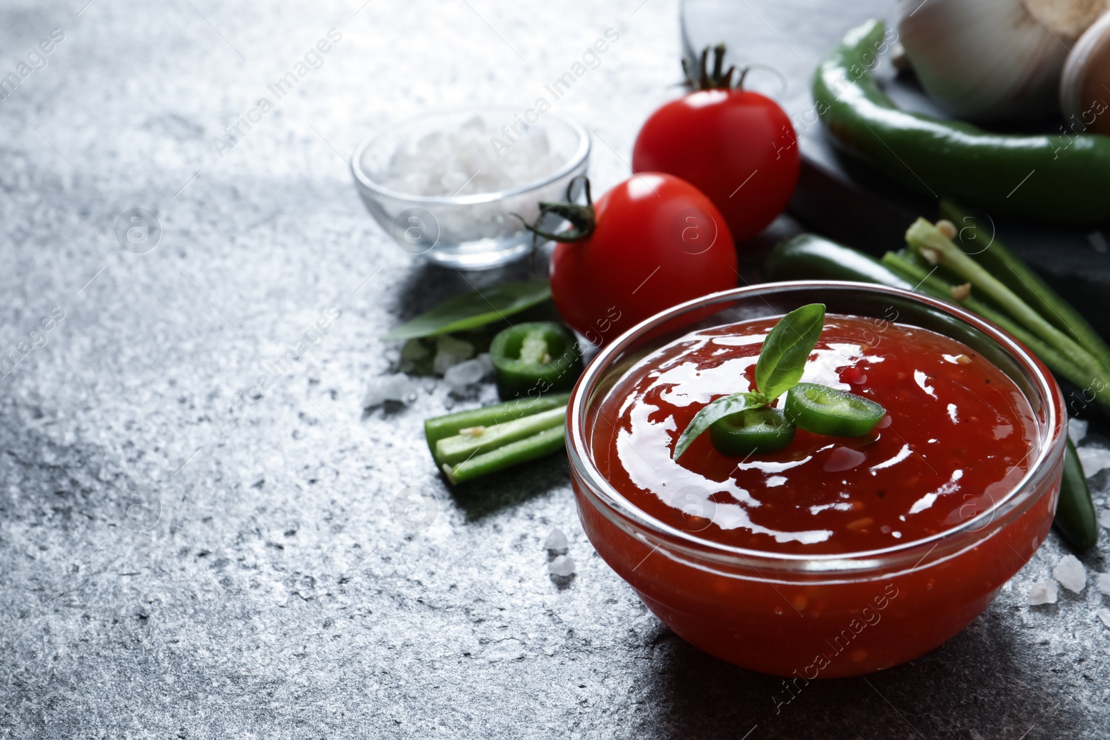 Photo of Spicy chili sauce in glass bowl on grey table, space for text