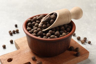 Photo of Aromatic allspice pepper grains in bowl and scoop on grey table, closeup
