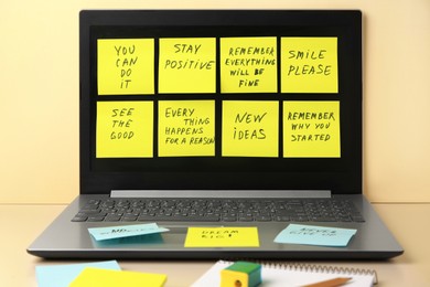 Photo of Paper notes with life-affirming phrases and laptop on table against beige background
