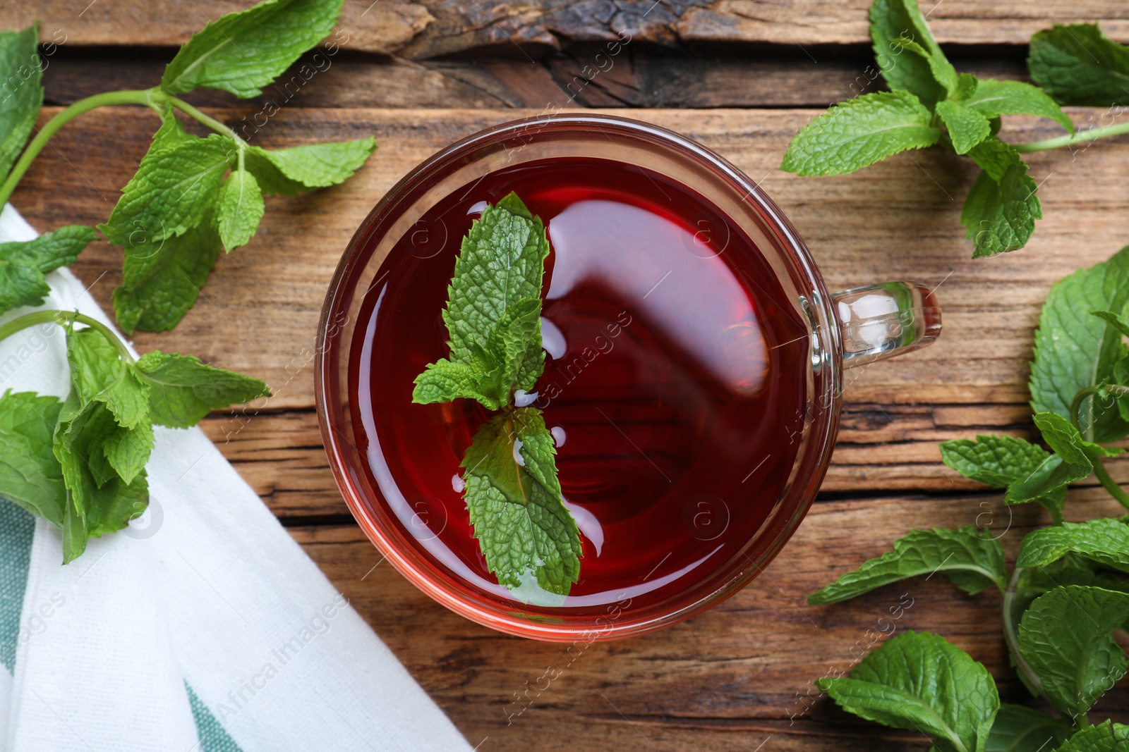 Photo of Cup with hot aromatic mint tea and fresh leaves on wooden table, flat lay