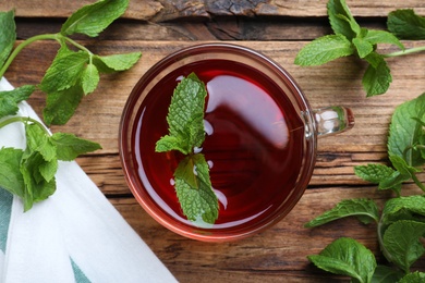 Photo of Cup with hot aromatic mint tea and fresh leaves on wooden table, flat lay