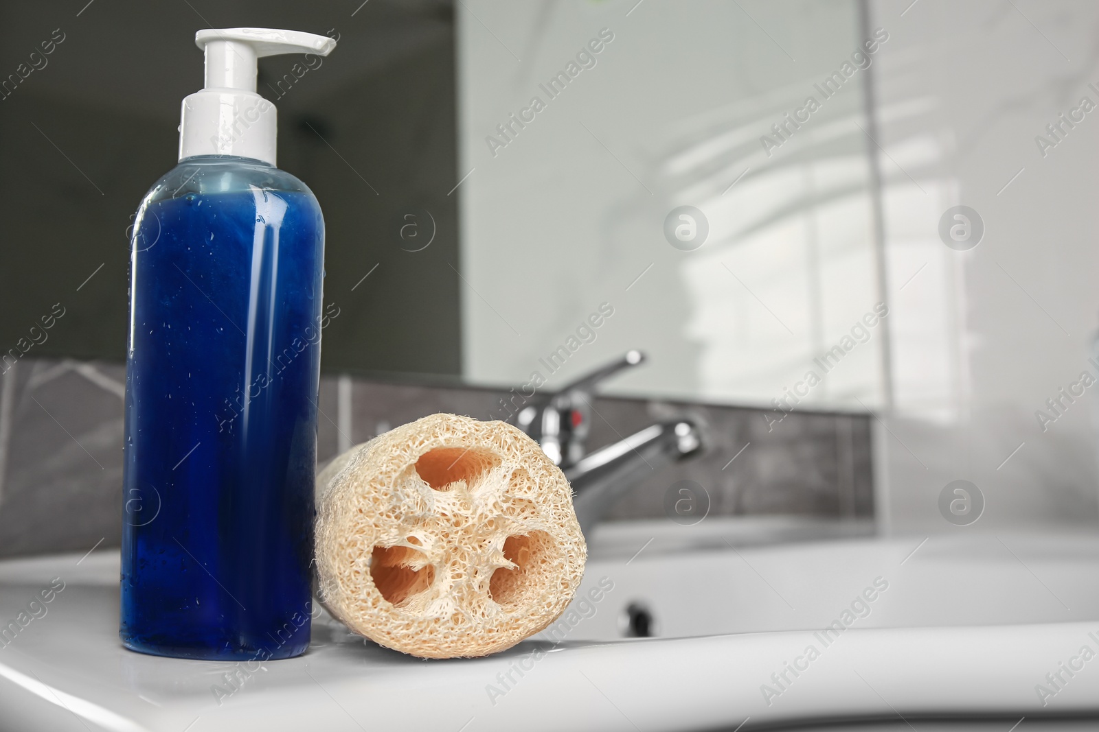 Photo of Natural loofah sponge and bottle with shower gel on washbasin in bathroom, closeup. Space for text