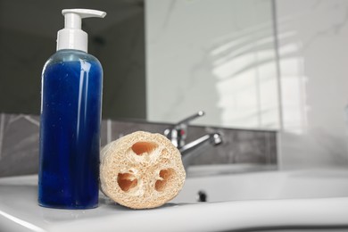 Natural loofah sponge and bottle with shower gel on washbasin in bathroom, closeup. Space for text