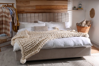 Bed with white knitted plaid in room. Interior design