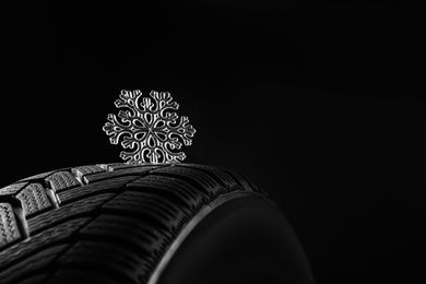 Photo of Winter tire with icy snowflake on black background, closeup. Space for text