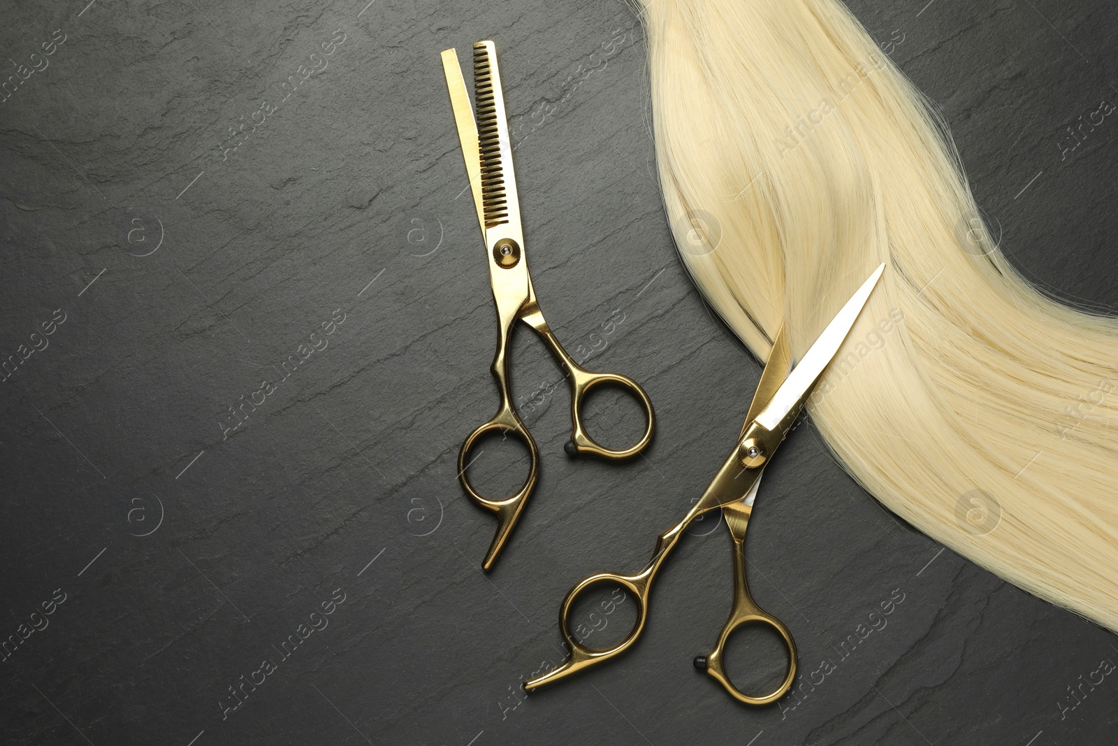 Photo of Professional hairdresser scissors with blonde hair strand on dark grey table, flat lay. Space for text
