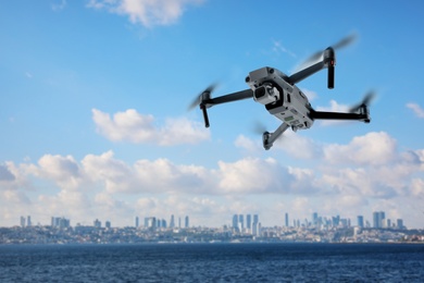 Image of Modern drone flying over sea and blurred cityscape on background. Aerial survey