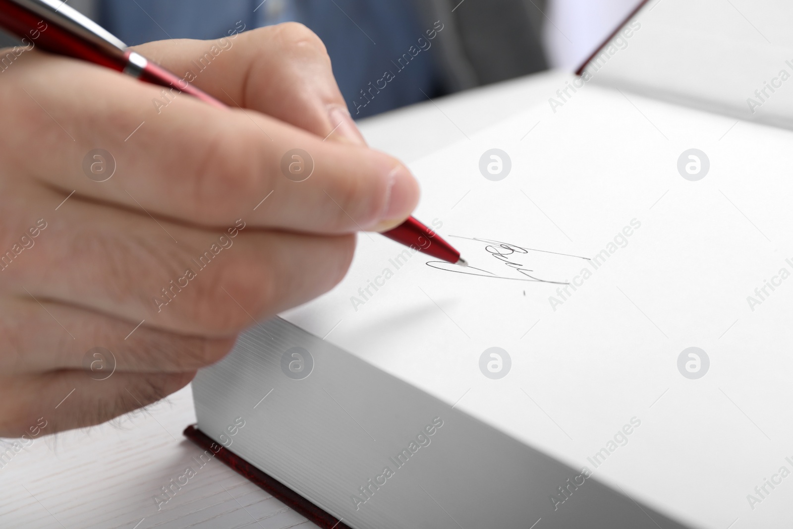 Photo of Writer signing autograph in book at table, closeup