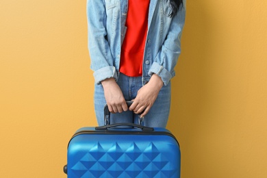 Young woman with suitcase on color background