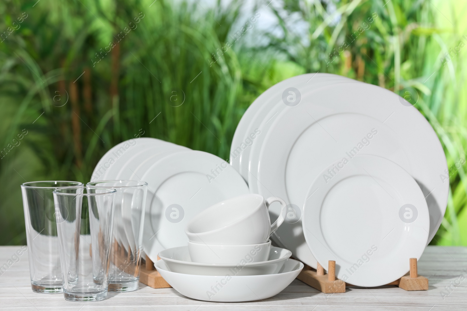 Photo of Set of clean dishware on white table against blurred background