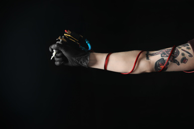 Photo of Tattoo artist with professional machine on black background, closeup