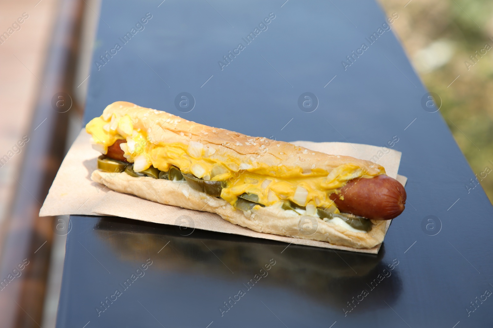 Photo of Fresh tasty hot dog with sauce on dark parapet outdoors