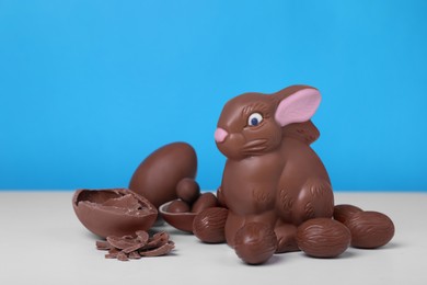Photo of Chocolate Easter bunny and eggs on white table against light blue background