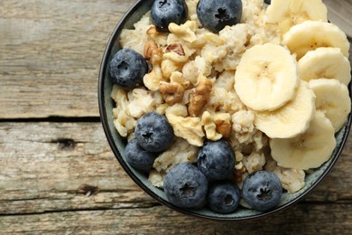 Photo of Tasty oatmeal with banana, blueberries and walnuts served in bowl on wooden table, top view. Space for text
