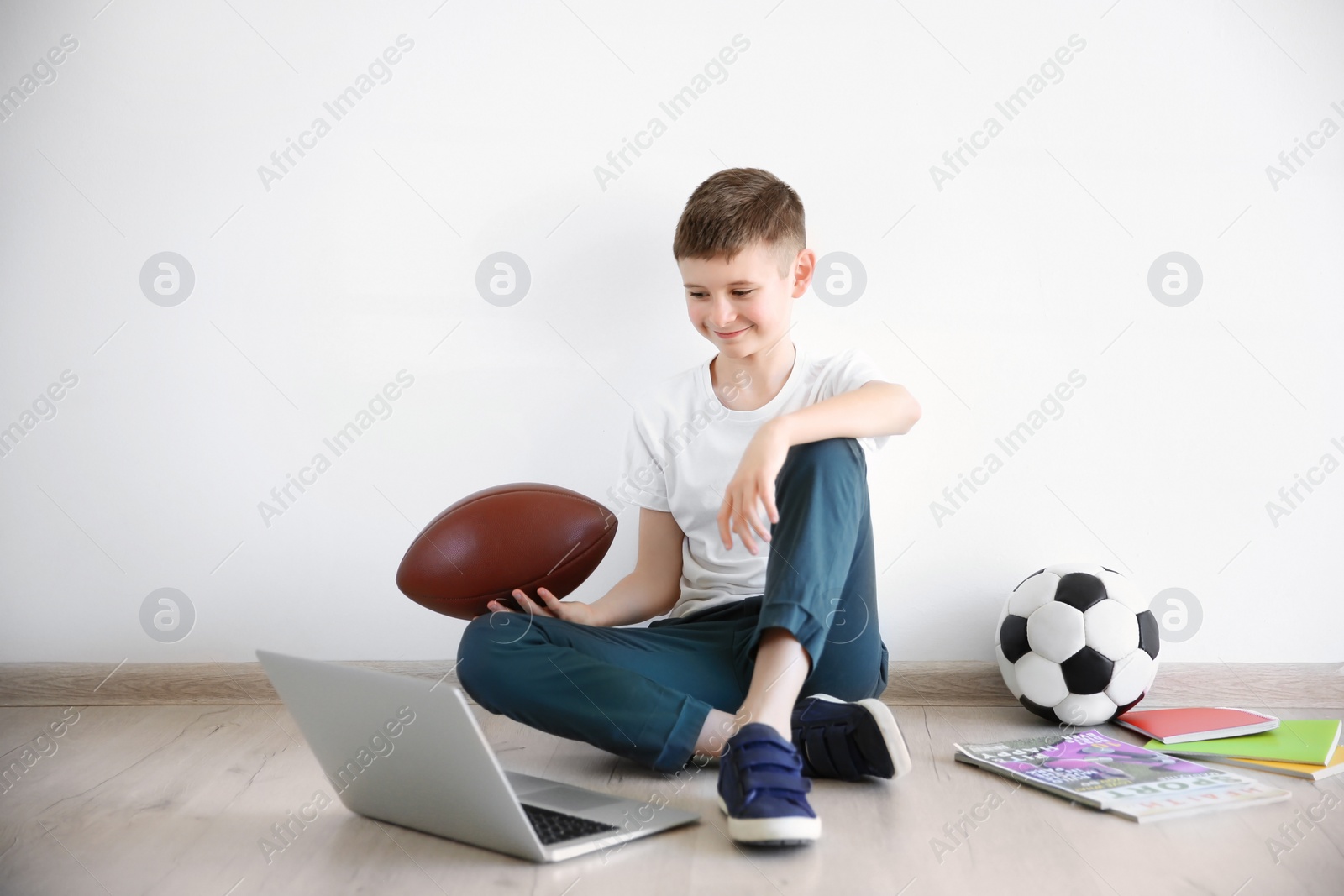 Photo of Cute little blogger with laptop and ball sitting on floor against light wall