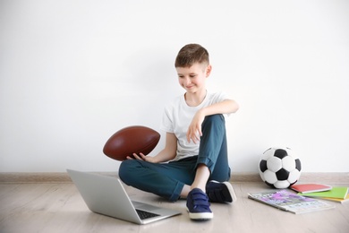 Cute little blogger with laptop and ball sitting on floor against light wall
