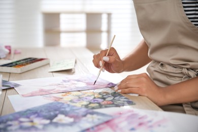 Photo of Young woman drawing flowers at table indoors, closeup. Space for text