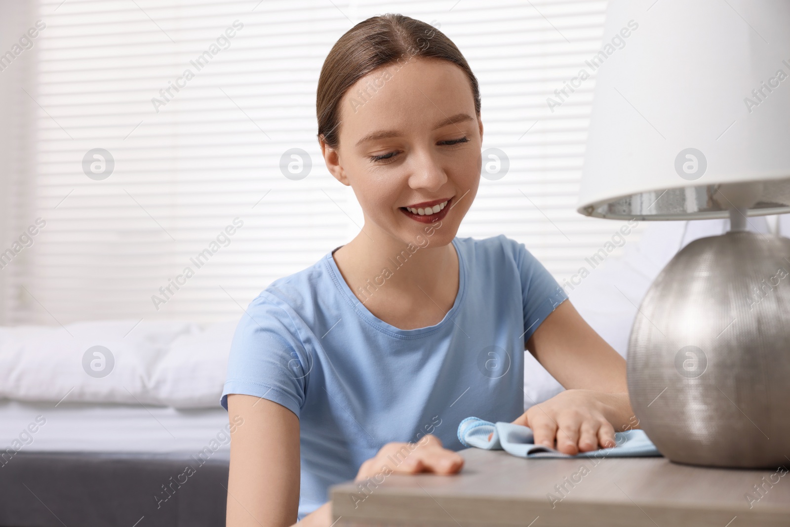 Photo of Woman with microfiber cloth cleaning wooden chest of drawers in room