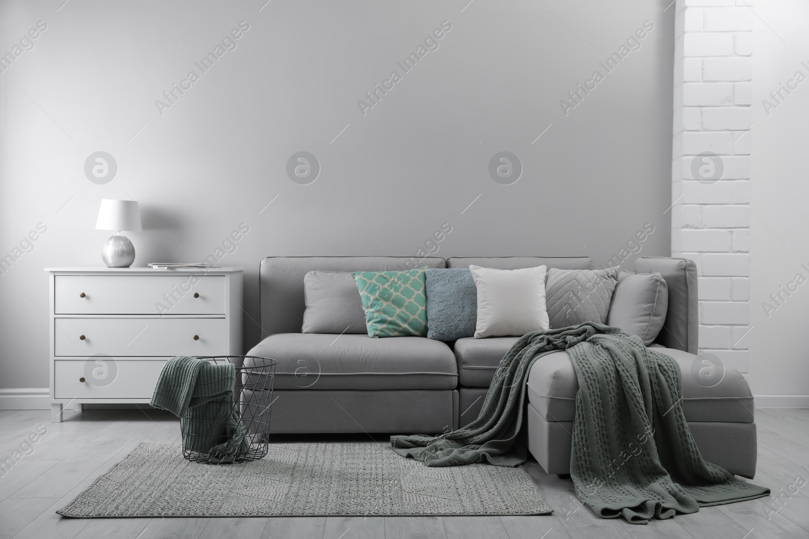 Photo of Large grey sofa and chest of drawers near light wall in room. Interior design