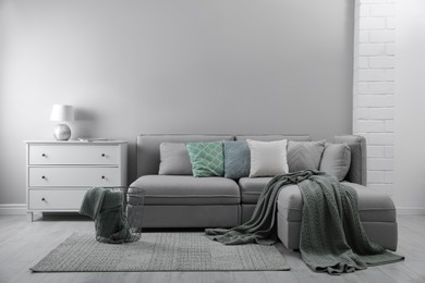 Large grey sofa and chest of drawers near light wall in room. Interior design