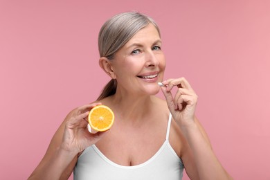 Photo of Beautiful woman with half of orange taking vitamin capsule on pink background