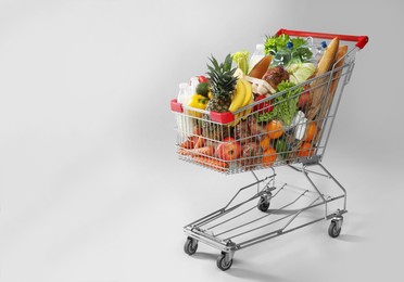 Photo of Shopping cart full of groceries on grey background. Space for text
