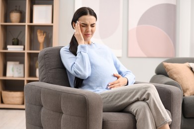 Pregnant woman suffering from headache on armchair at home