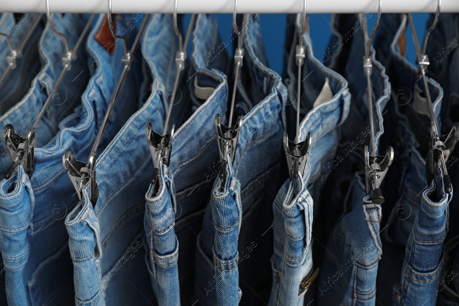 Photo of Hangers with stylish jeans on rack, closeup