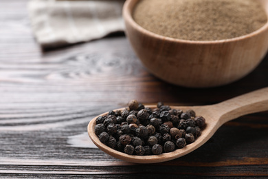 Photo of Peppercorns in spoon on wooden table, closeup