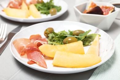 Photo of Plate with melon slices, prosciutto and olives on gray table