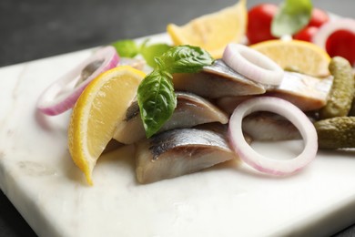 Serving board with sliced salted herring fillet, basil, onion rings, pickles and lemon on table, closeup