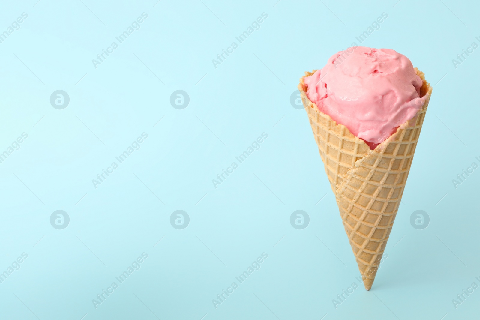 Photo of Delicious pink ice cream in waffle cone on light blue background. Space for text