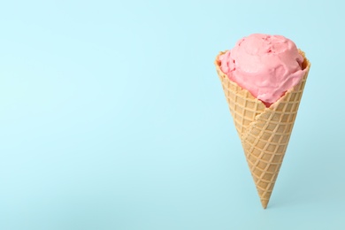 Photo of Delicious pink ice cream in waffle cone on light blue background. Space for text