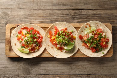 Delicious tacos with vegetables, green onion, lime and ketchup on wooden table, top view