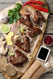 Tasty chicken wings glazed in soy sauce with garnish on wooden table, flat lay