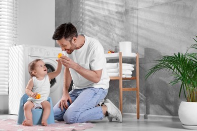 Photo of Father training his child to sit on baby potty indoors. Space for text