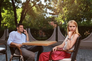 Photo of Man talking on phone and ignoring his girlfriend in outdoor cafe. Boring date
