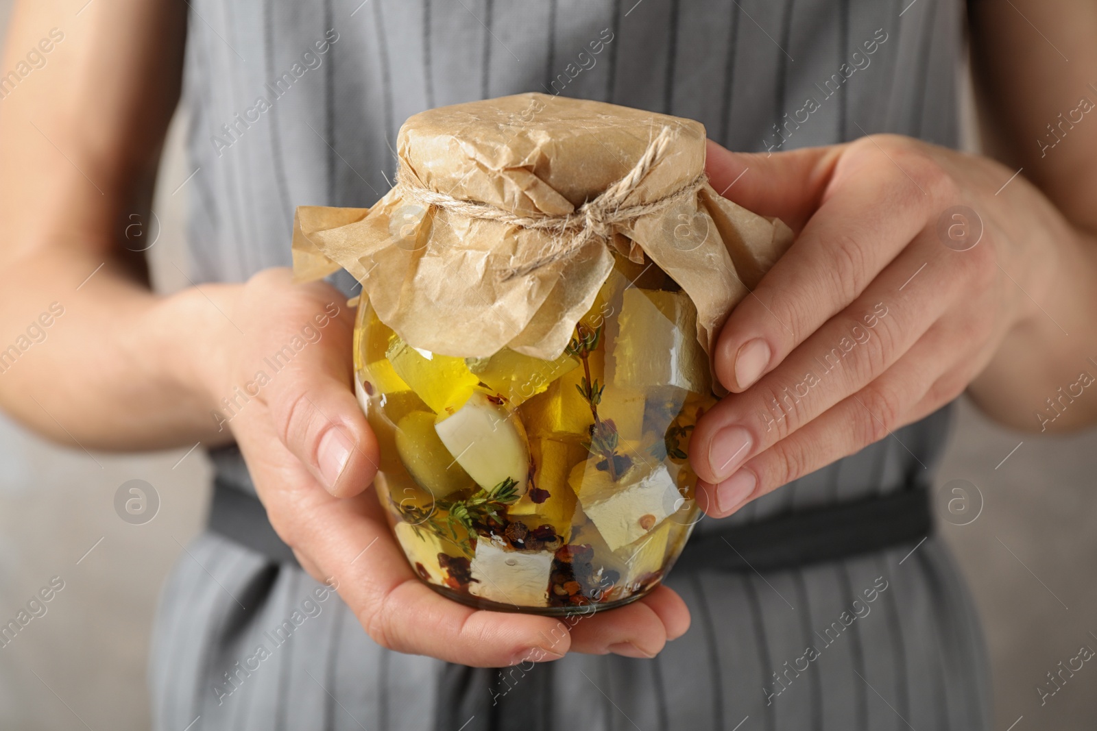 Photo of Woman holding jar with pickled feta cheese on beige background, closeup