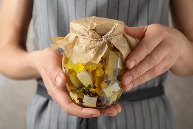 Photo of Woman holding jar with pickled feta cheese on beige background, closeup