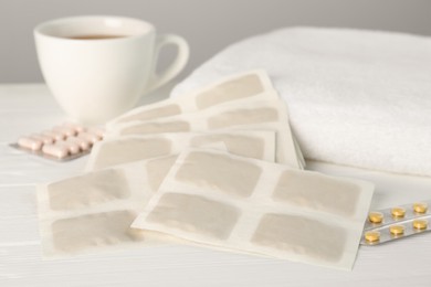 Photo of Mustard plasters, pills, towel and tea on white wooden table, closeup
