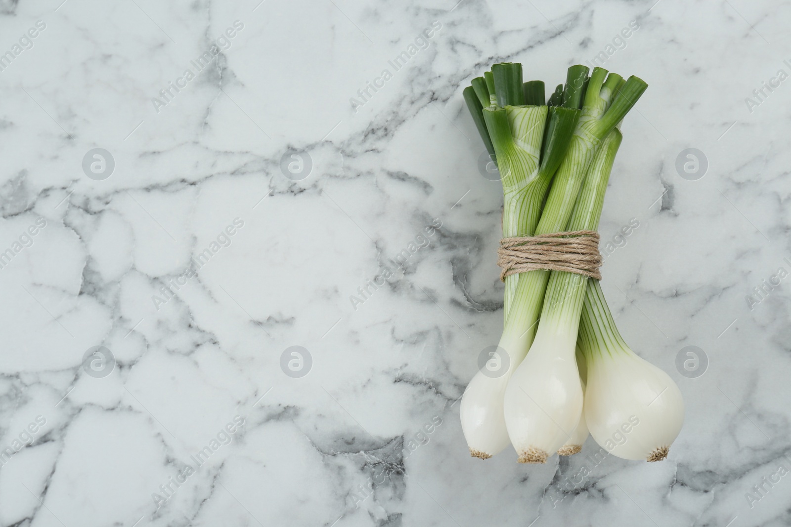 Photo of Bunch of green spring onions on white marble table, flat lay. Space for text